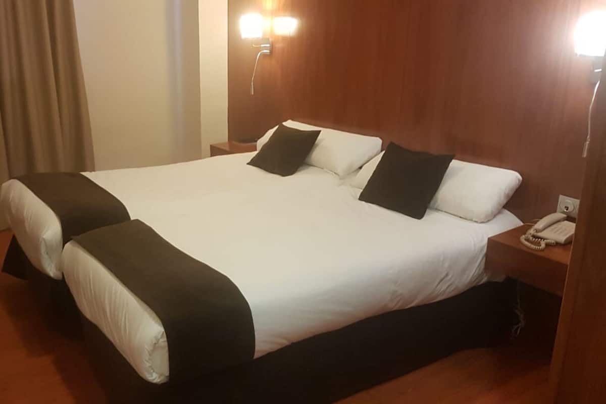 Una habitación de hotel con una cama grande, dos mesitas de noche, un teléfono y una lámpara fijada a la pared.