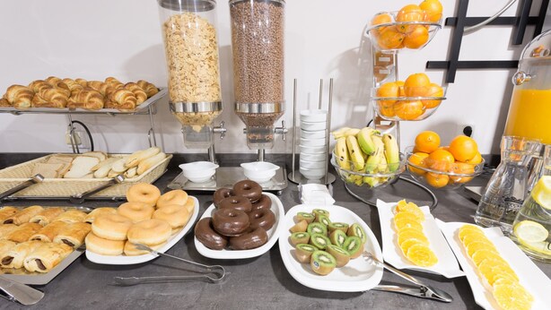 A buffet with various food items including pastries, donuts, and fresh fruits.