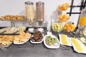 Un buffet proposant une variété de plats, notamment des pâtisseries, des beignets et des fruits frais.