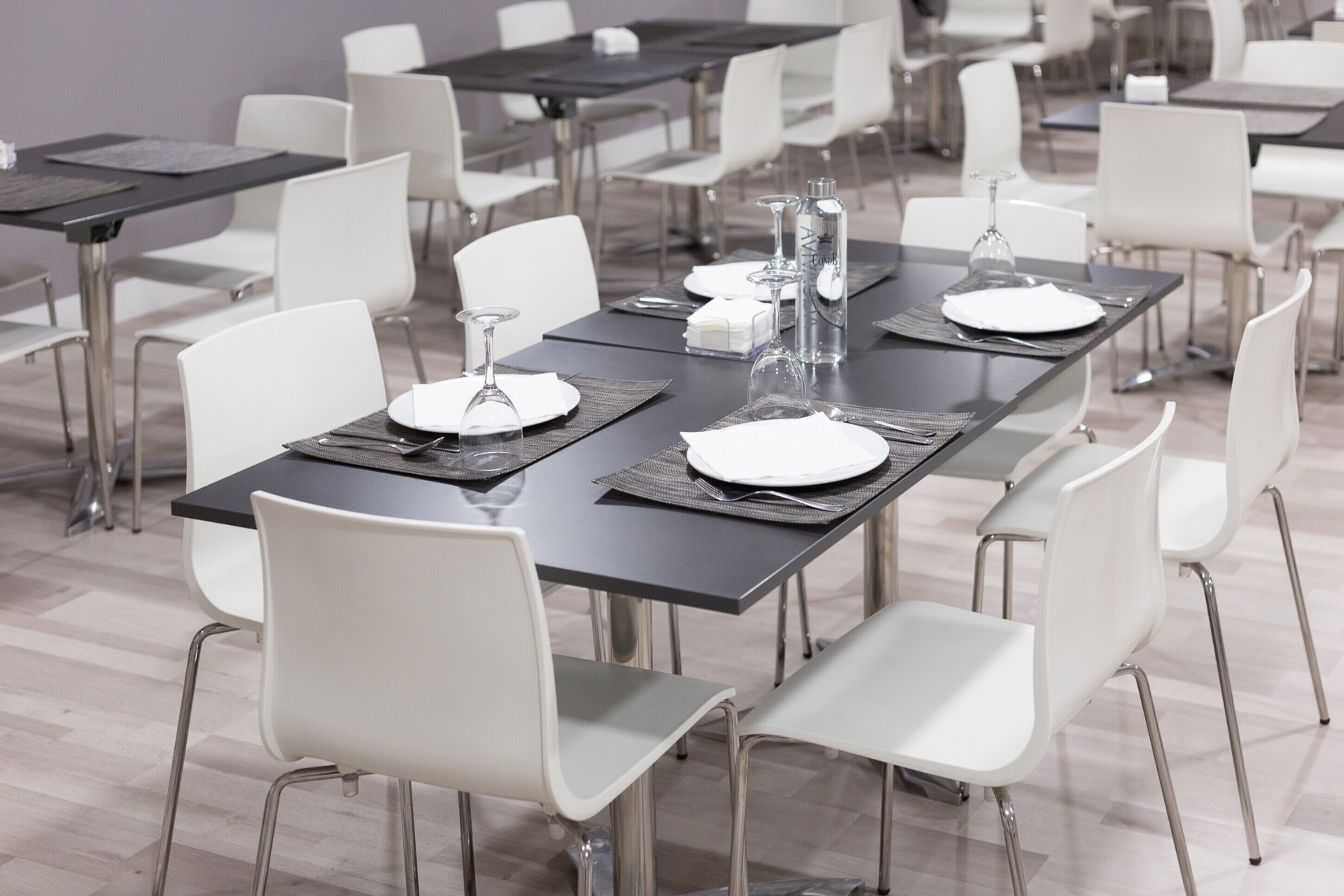 A conference room with rectangular tables, white chairs, and black placemats.