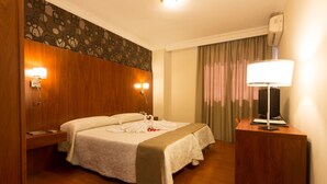 A hotel room with a bed, bedside tables, a desk, a lamp, and a television.