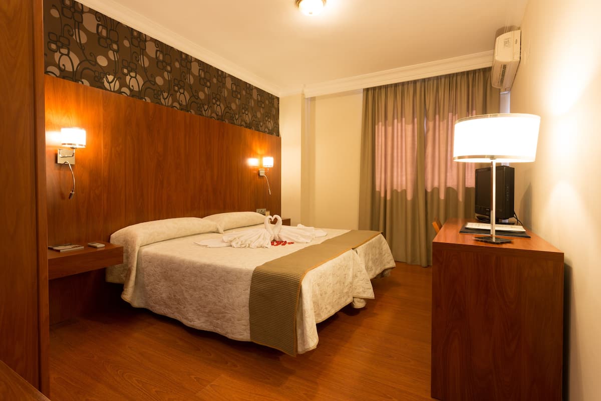 Una habitación de hotel con cama, mesitas de noche, escritorio, lámpara y televisor.
