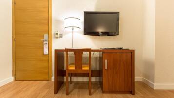 Habitación pequeña con un escritorio de madera, una silla, un televisor montado en la pared y una puerta.