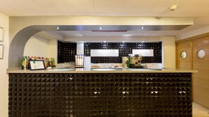 A reception area with a black, geometric-patterned counter, a coffee machine, and a variety of bottled beverages.