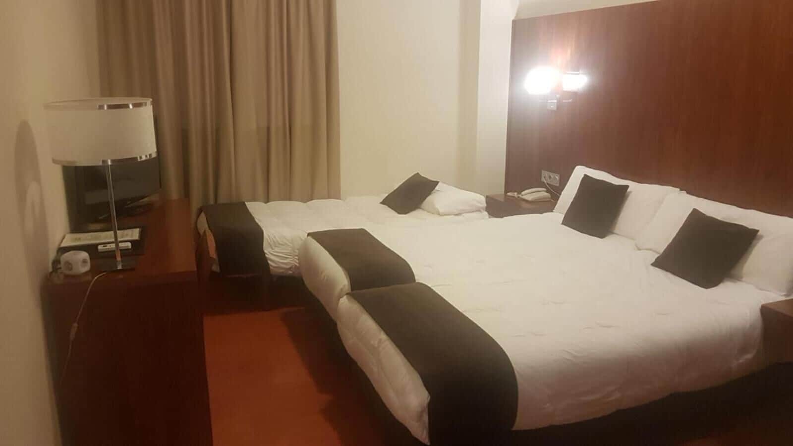 A hotel room with two beds, a desk with a lamp, and a telephone.
