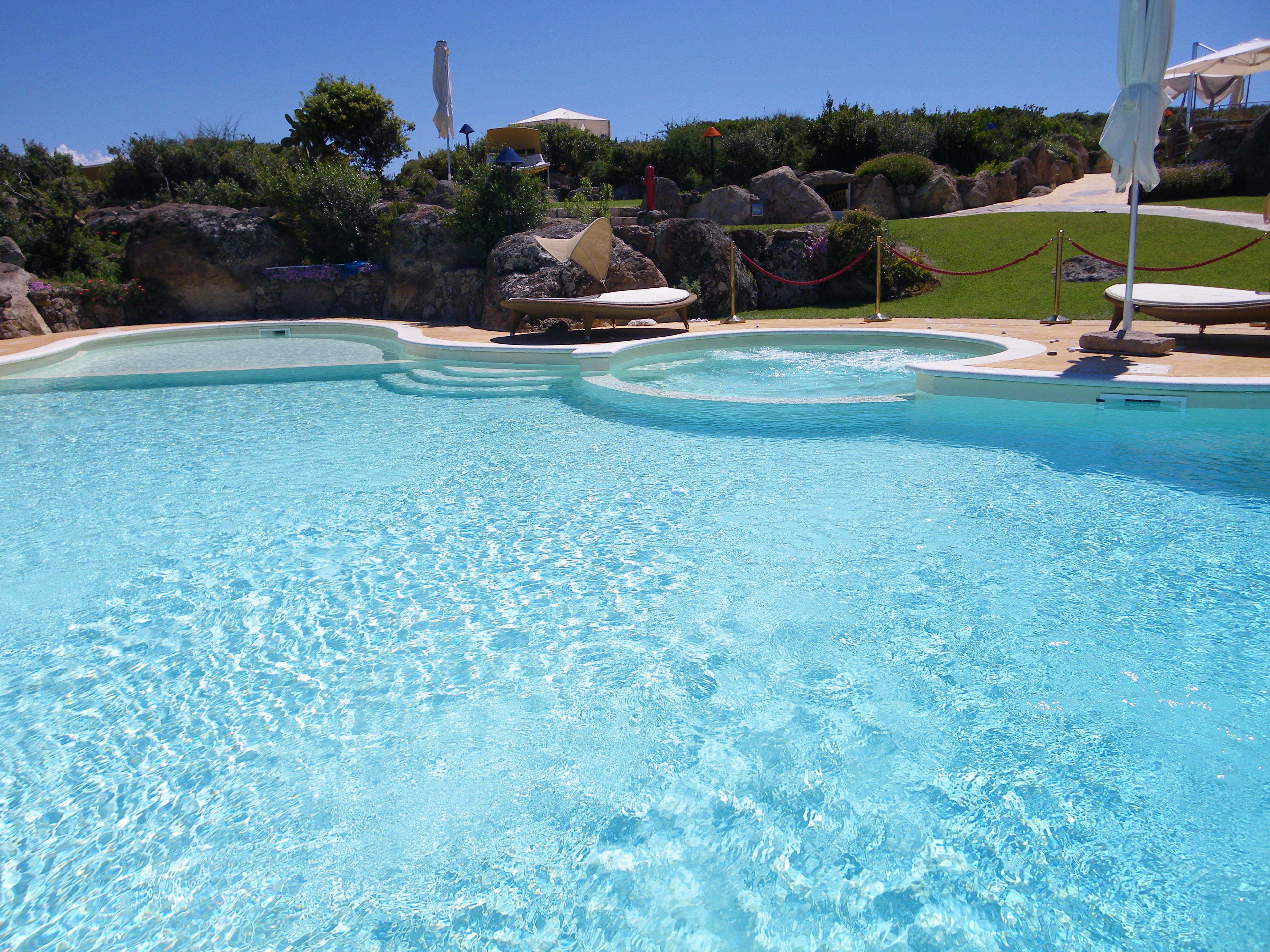 Una piscina azul cristalina con diseño curvo, rodeada de rocas y vegetación.