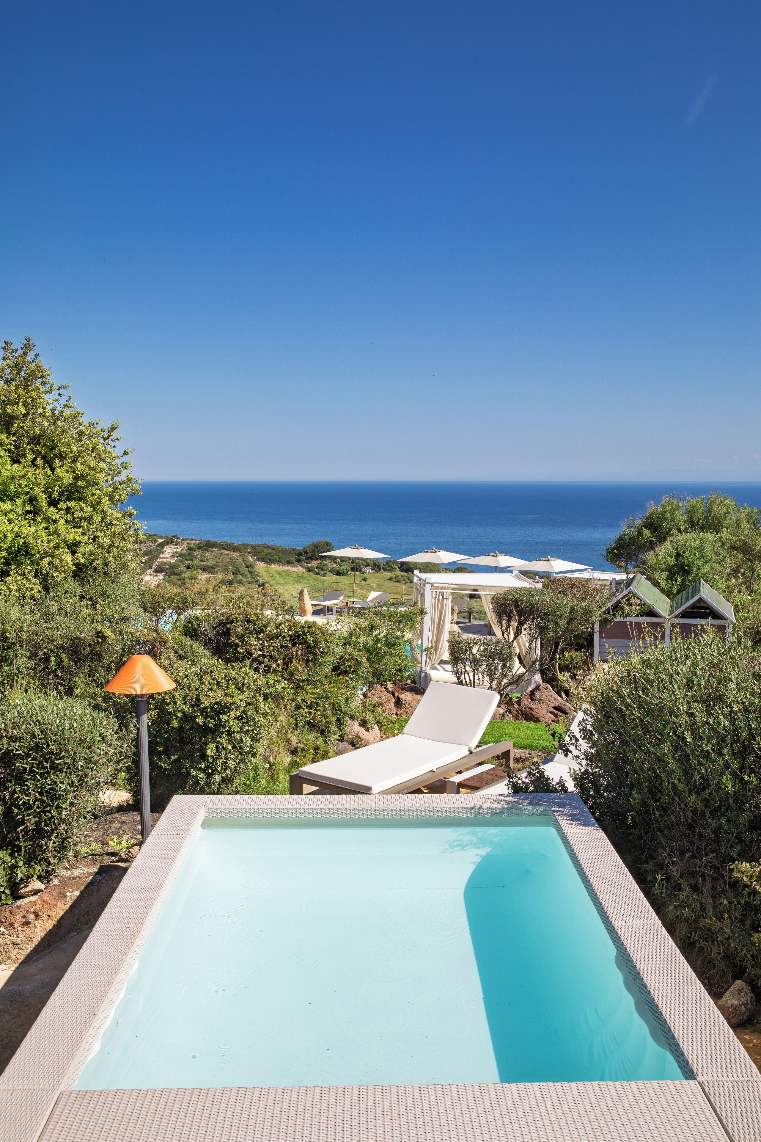A swimming pool with a view of the ocean, surrounded by greenery and a gazebo.