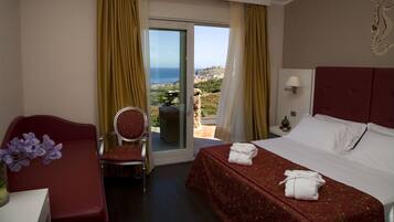 A hotel room with a bed, a desk, a chair, and a view of the sea.