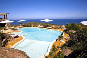 Una piscina con vista al océano, rodeada de sillas de descanso y sombrillas.