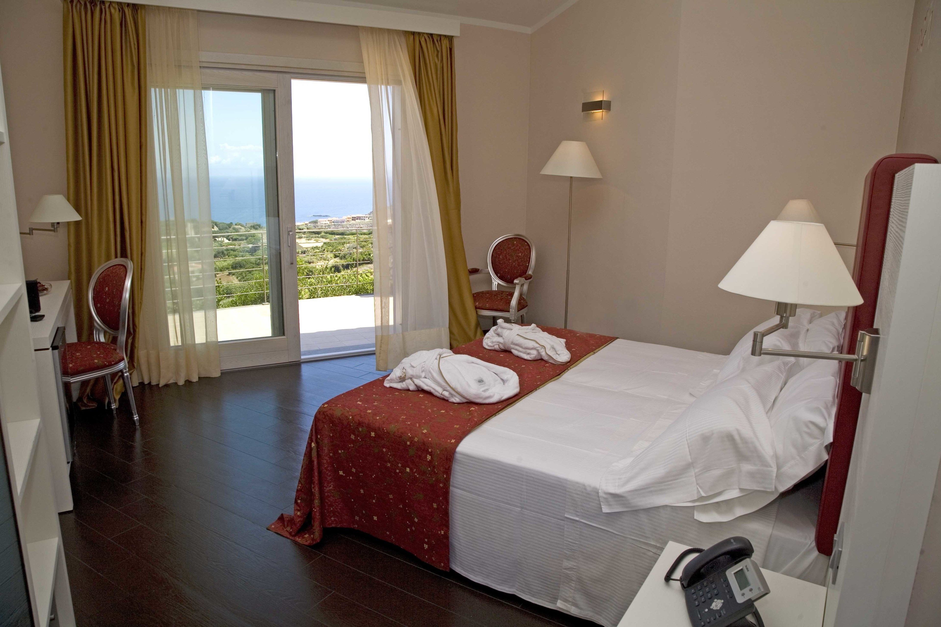 A hotel room with a bed, a chair, a desk with a phone, and a view of the outdoors.