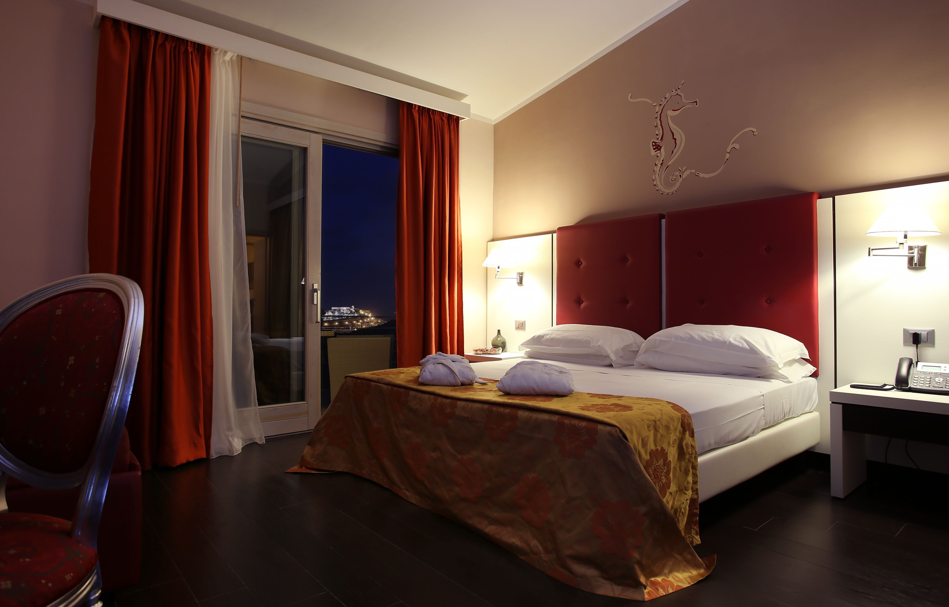 Une chambre d’hôtel avec un lit, un bureau avec un téléphone, une chaise et une vue à travers une porte vitrée.