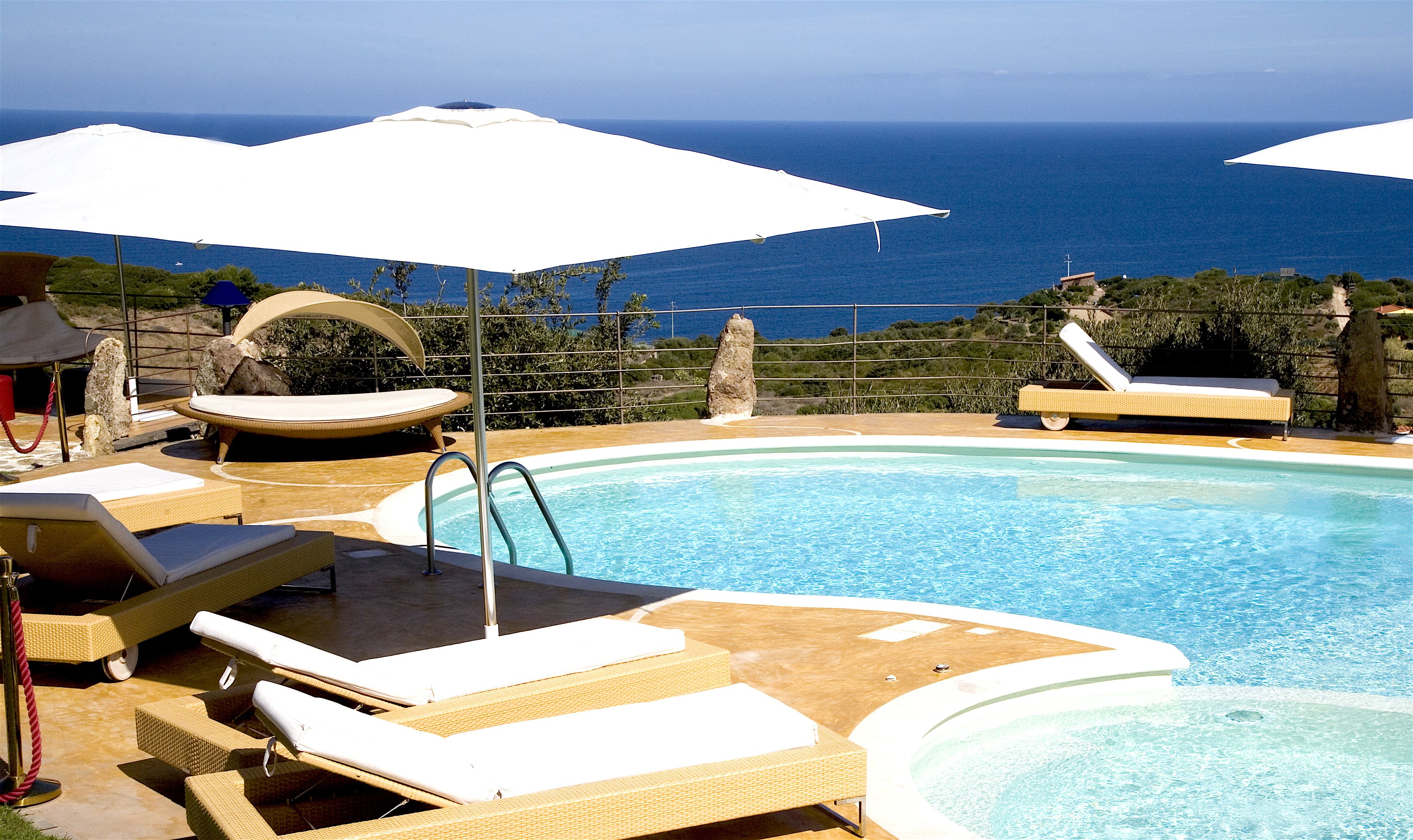 A pool area with lounge chairs and umbrellas, overlooking a body of water.