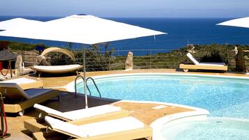 A pool area with lounge chairs and umbrellas, overlooking a body of water.