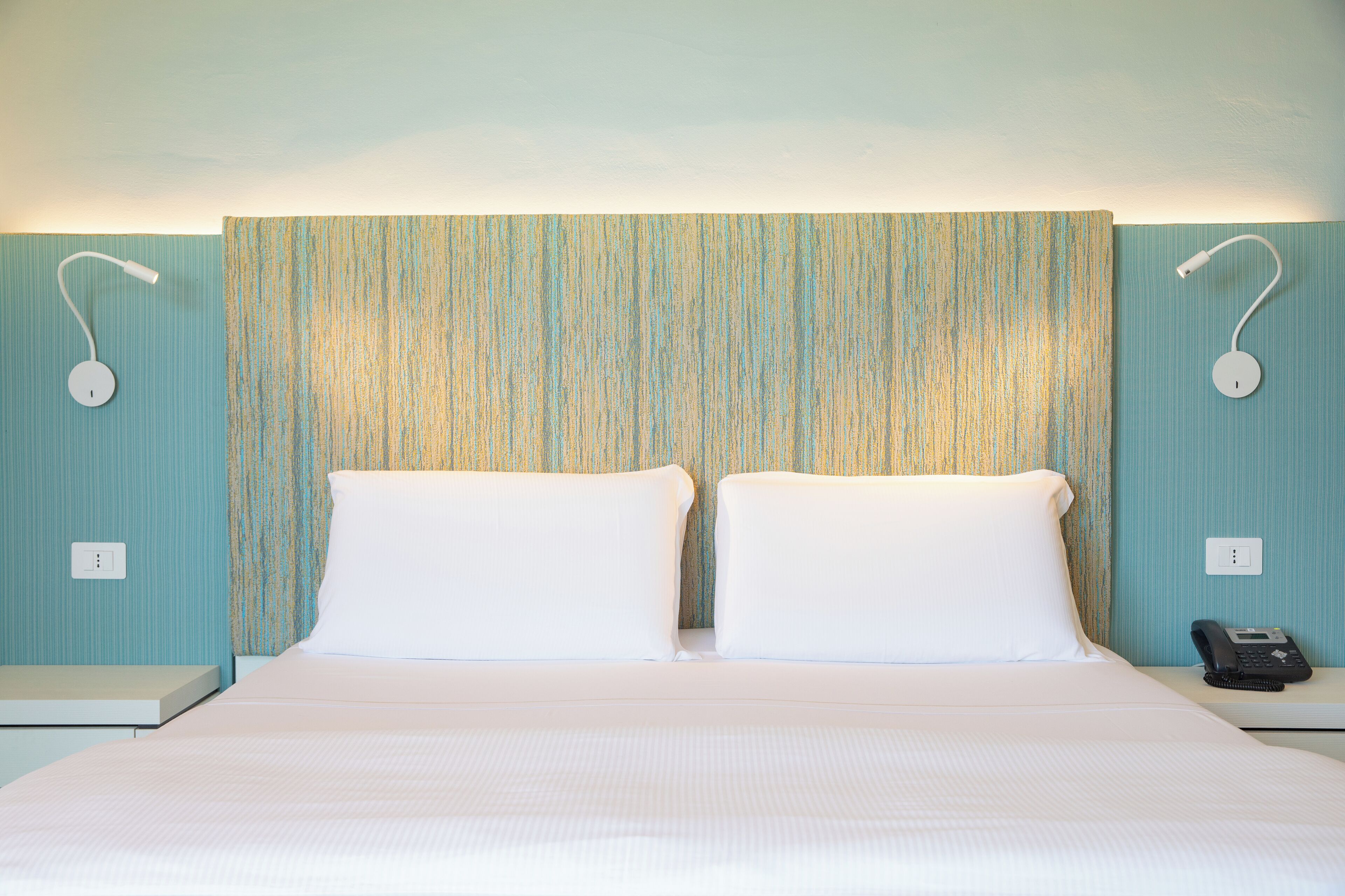 A hotel room with a bed, two bedside tables, a telephone, and a wall with a textured pattern.