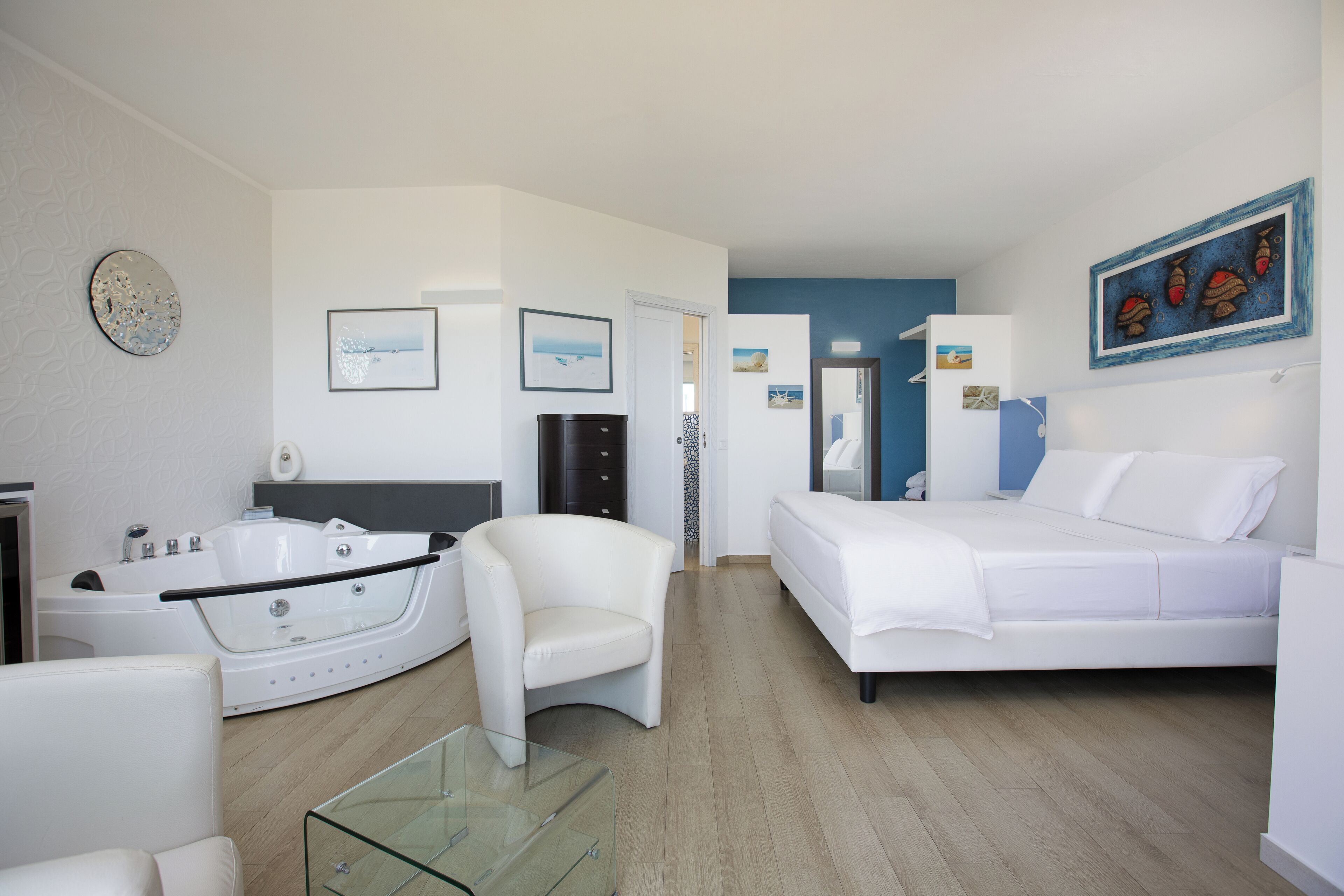 Ein modernes Hotelzimmer mit einer großen Badewanne, einem weißen Sofa, einem Glastisch und einem Bett.