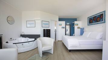 Ein modernes Hotelzimmer mit einer großen Badewanne, einem weißen Sofa, einem Glastisch und einem Bett.