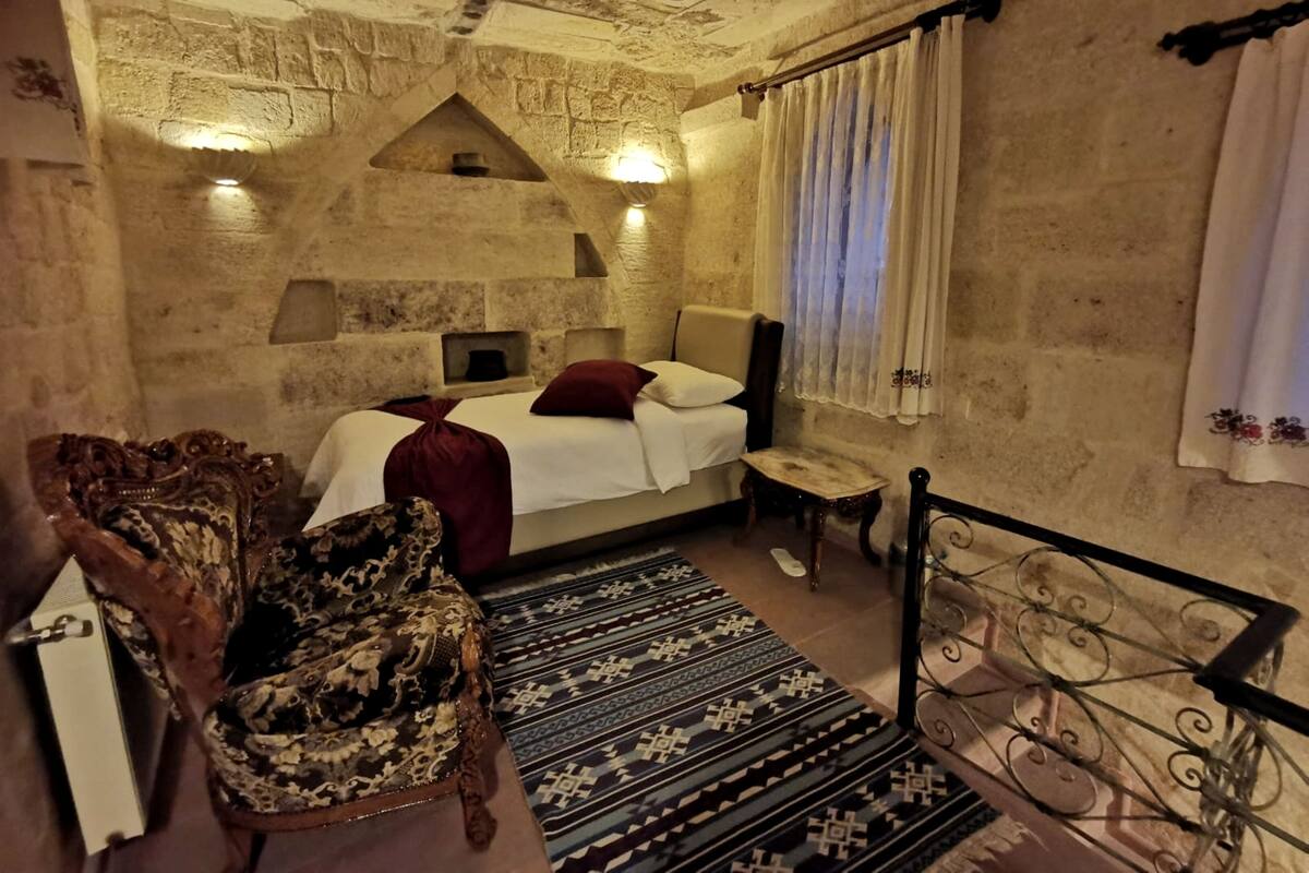 A bedroom with a bed, a chair, a small table, and a decorative metal railing.