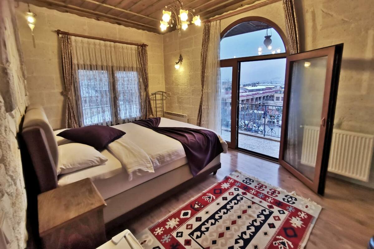 A bedroom with a bed, a window with curtains, a view of a cityscape, and a patterned rug.