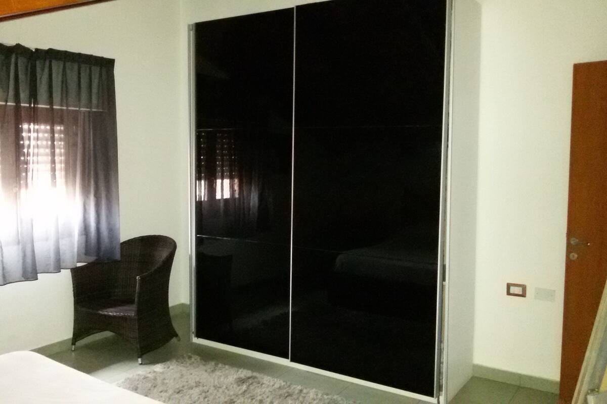 A room with a bed, a chair, a sliding door, and a window with curtains.