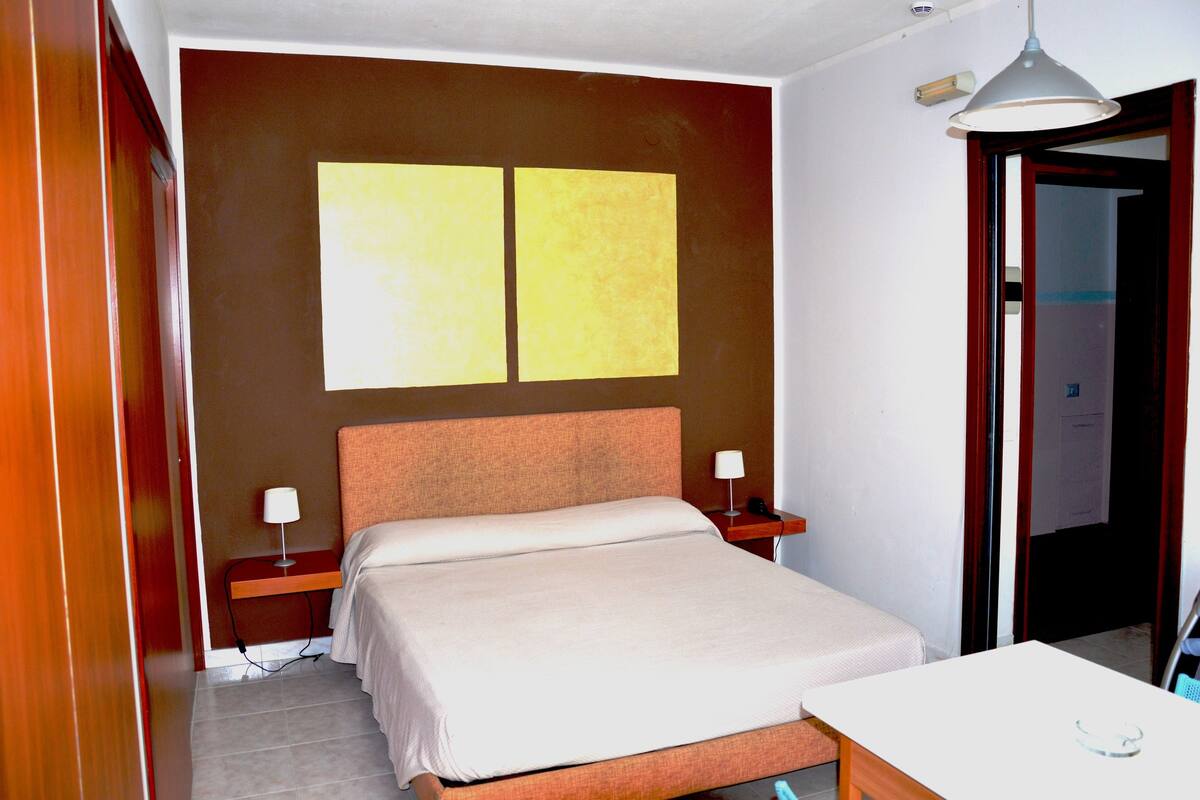 A hotel room with a bed, bedside tables, a desk, and a lamp.