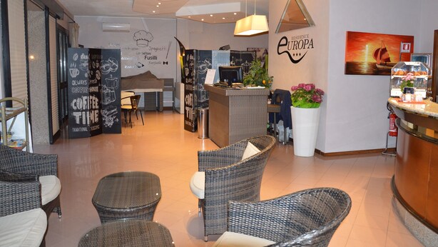 Een modern koffiehuis interieur met rieten meubels, een balie met een menu en een schilderij van een zonsondergang aan de muur.