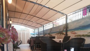 Een terras buiten met rieten meubilair, een betegelde vloer en een muurschildering van een strand.