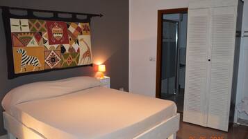 A bedroom with a bed, a nightstand with a lamp, a wall with a colorful tapestry, and a closet.