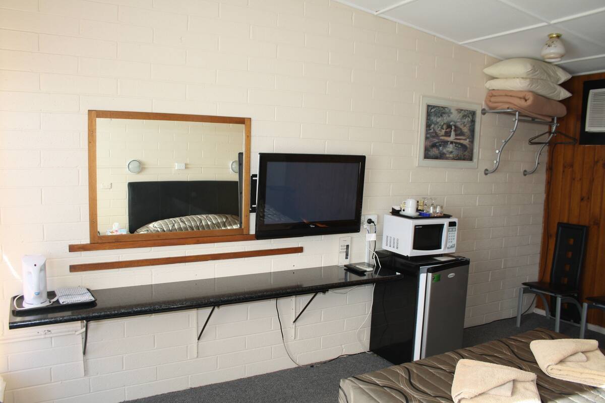 A hotel room with a bed, a desk with a computer, a television, a microwave, and a small refrigerator.