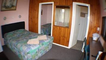 A bedroom with a bed, a desk, and two doors leading to other rooms.