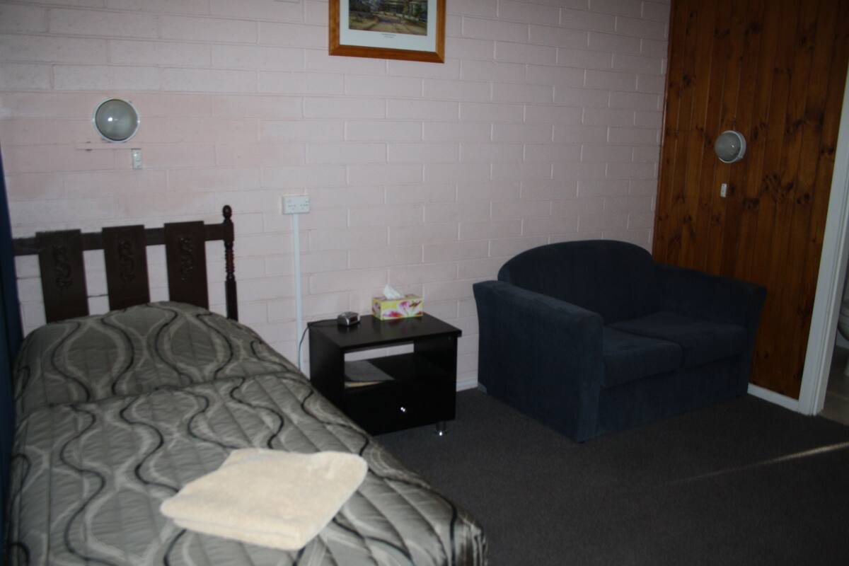 A bedroom with a bed, a chair, a nightstand, and a door.