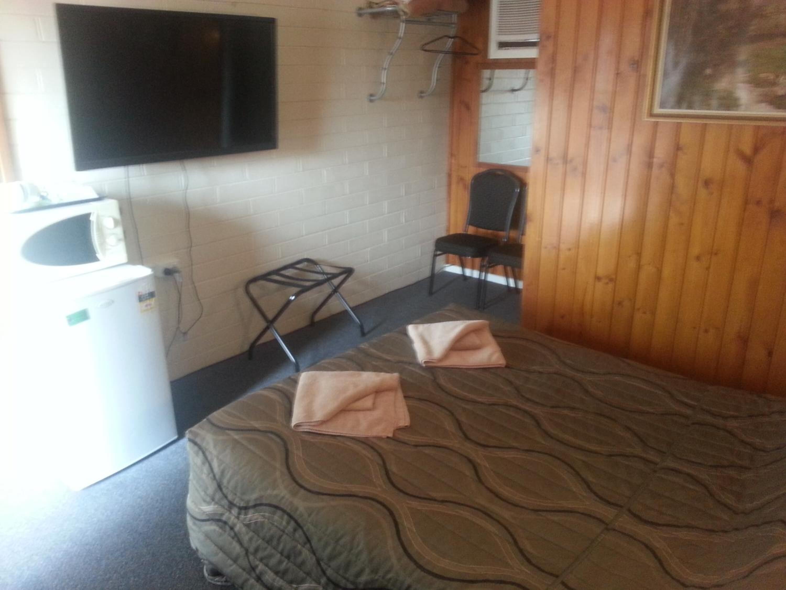 A room with a bed, a small table, a chair, a TV mounted on the wall, and a window.