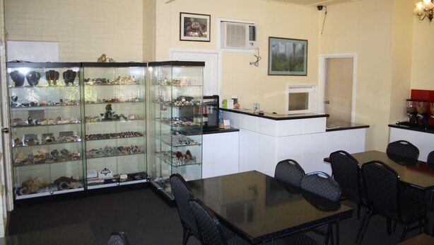 A dining area with a glass display case filled with various items, a black table with chairs, and a white wall with framed pictures and an air conditioning unit. - Nhill Oasis Motel (Nhill)