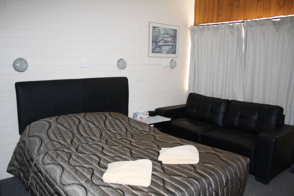 A hotel room with a bed, a black leather sofa, a small table, and a painting on the wall.
