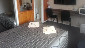 A hotel room with a bed, a desk with a chair, a television, and a bathroom visible through an open door. - Nhill Oasis Motel (Nhill)