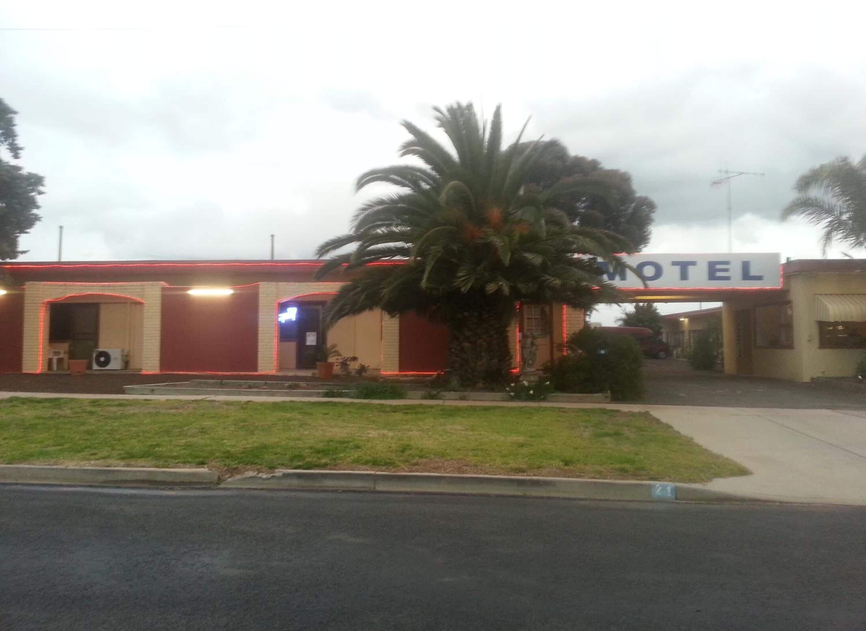 A motel with a signboard, a palm tree, and a building with red and beige exterior walls.
