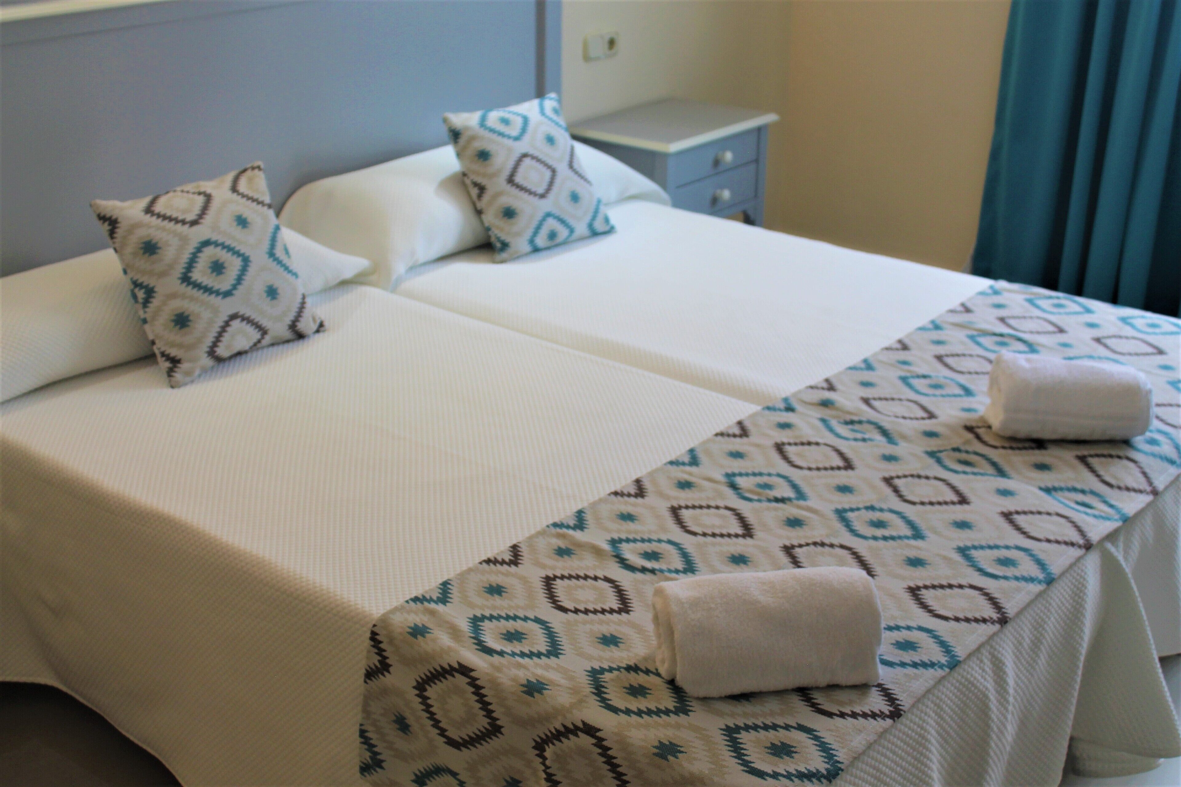 Une chambre d’hôtel avec deux lits, chacun recouvert d’une couvre-lit à motifs et agrémenté d’oreillers. On y trouve une table de chevet avec une lampe et un tiroir.
