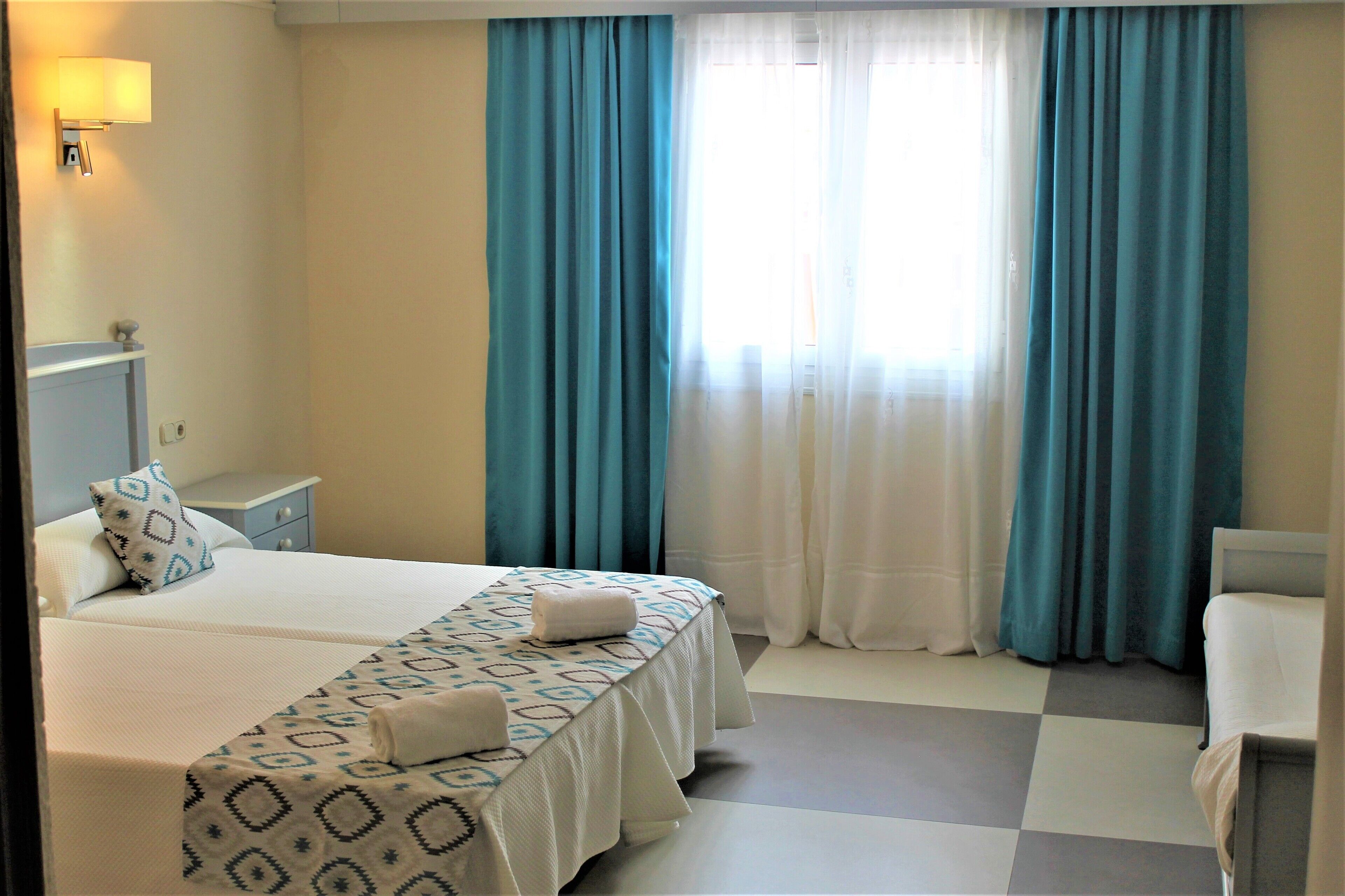 Une chambre d’hôtel avec deux lits, une table de chevet, une lampe et une vue sur l’extérieur à travers les rideaux.