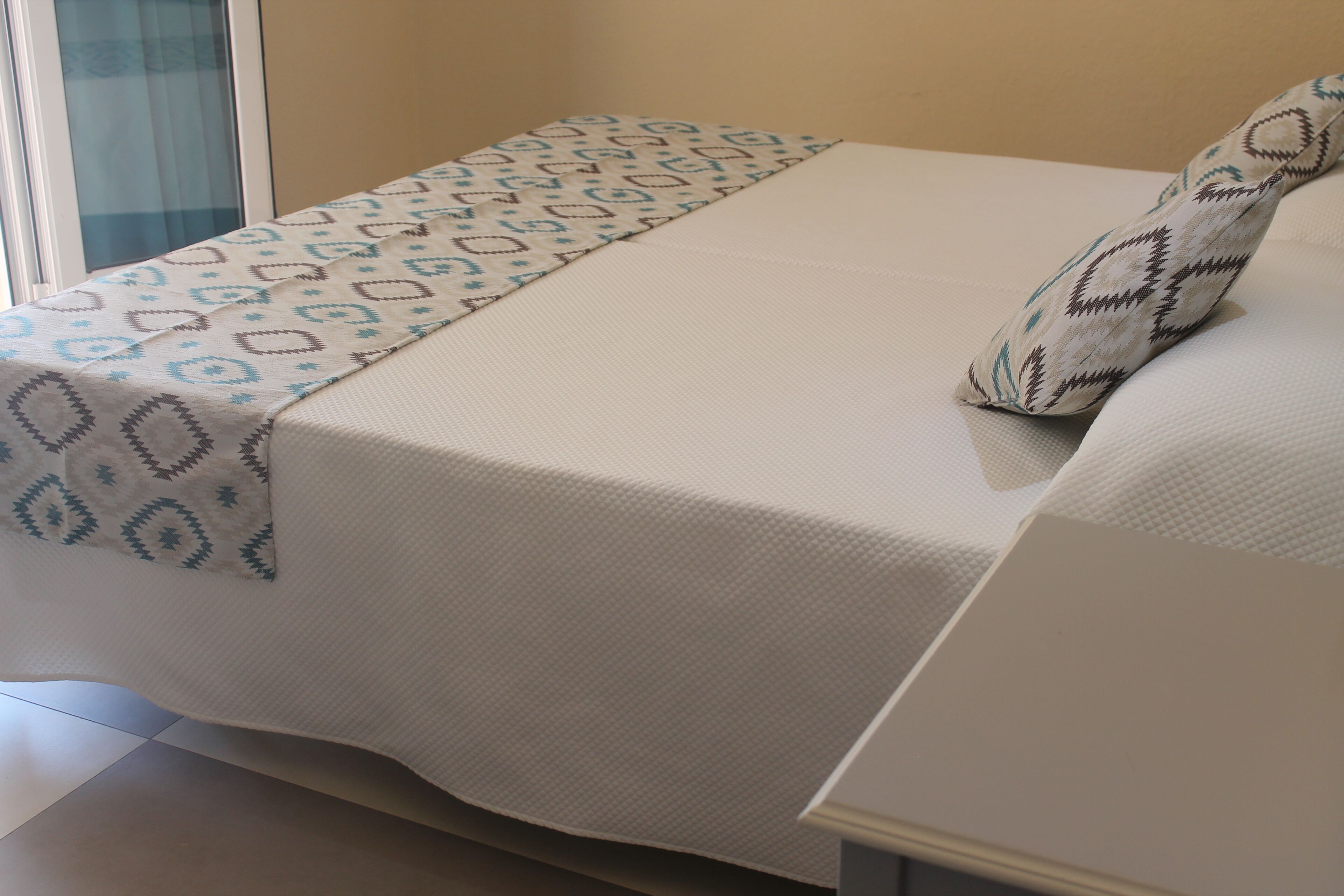 Een bed met een bedsprei met een patroon en een kussen met een geometrisch ontwerp.
