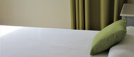 A hotel room with a bed, two pillows, a window, and curtains.