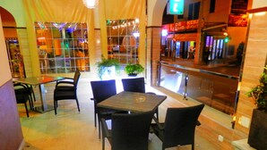 An indoor dining area with a glass partition, black wicker chairs, a wooden table, and potted plants. - Hotel Playa Sol (Palma de Mallorca)