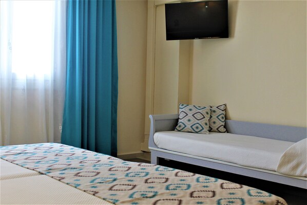 Habitación de hotel con cama, sofá, televisor montado en la pared y ventana con cortinas.