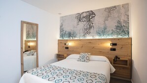A bedroom with a large bed, a wooden headboard, a wall mural, a bedside table, and a nightstand. - Hotel Playa Sol (Palma de Mallorca)