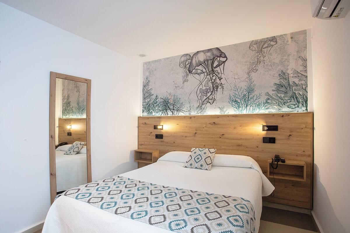 Ein Schlafzimmer mit einem großen Bett, einem Holz-Kopfteil, Wandmalerei, einem Nachttisch und einem Beistelltisch.