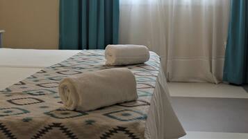 Une chambre d’hôtel avec un lit, une serviette roulée posée sur le lit et une fenêtre avec des rideaux.