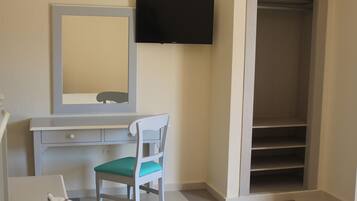Une pièce comprenant un bureau, une chaise, un miroir, une télévision et un dressing.