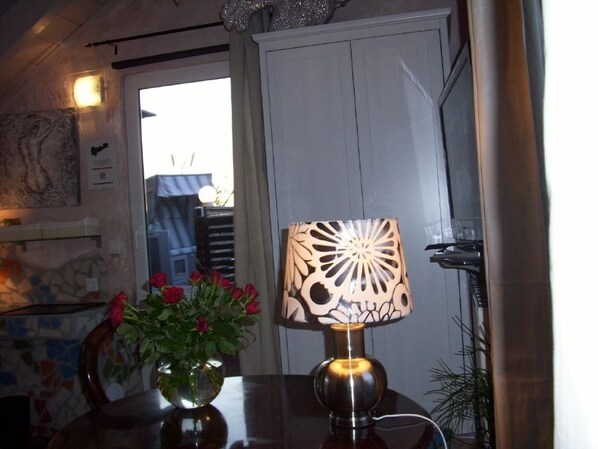 Una mesa con un jarrón de rosas rojas, una lámpara decorativa y vistas de una puerta y una ventana.