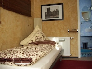 A bedroom with a bed, a framed picture on the wall, a radiator, and a bathroom visible through an open door. - Fritzi's Art Hotel (Filderstadt)
