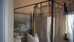 A four-poster bed with a canopy, white pillows, and a view of a cityscape through a window. - Fritzi's Art Hotel (Filderstadt)