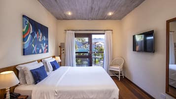 A bedroom with a large bed, a painting on the wall, a TV, and a view of the outdoors.