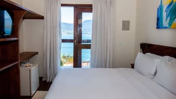 Un dormitorio con cama, televisión, refrigerador pequeño y vista al mar a través de una puerta.